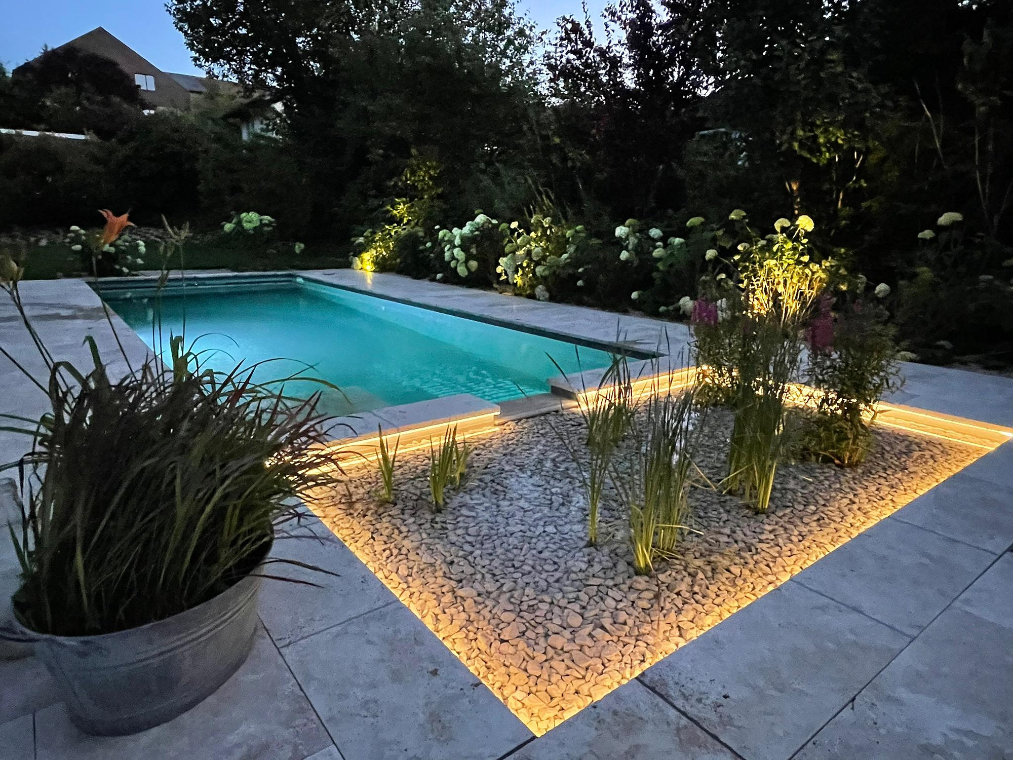 Beleuchteter Privatgarten bei Nacht: Pool, Kiesbeet mit Lichtlinie und angestrahlte Gräser