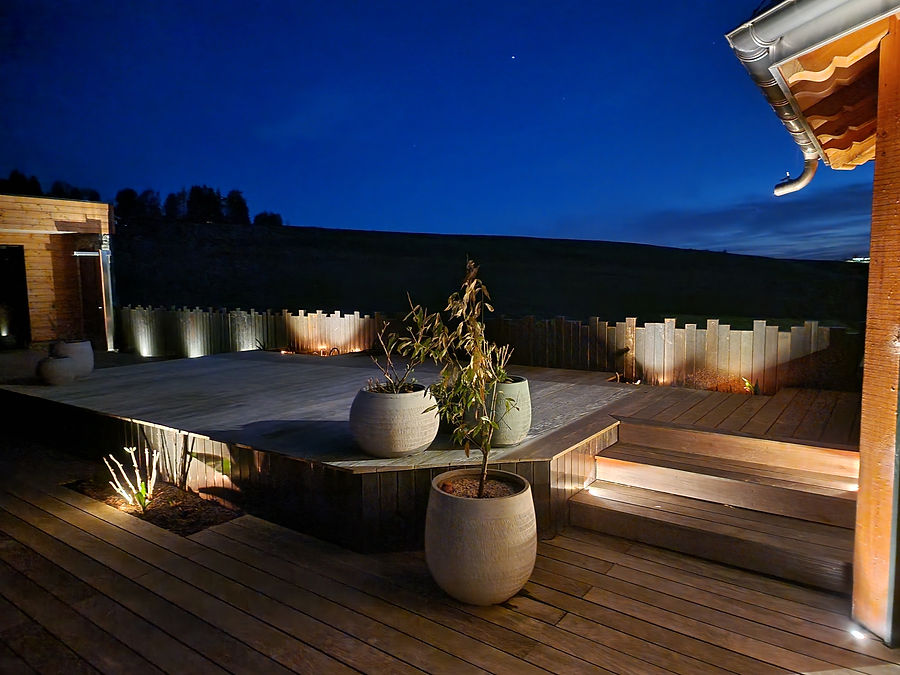 Terrassenbeleuchtung: Holzdeck mit beleuchteten Stufen, Pflanzgefässen und Holzpalisaden