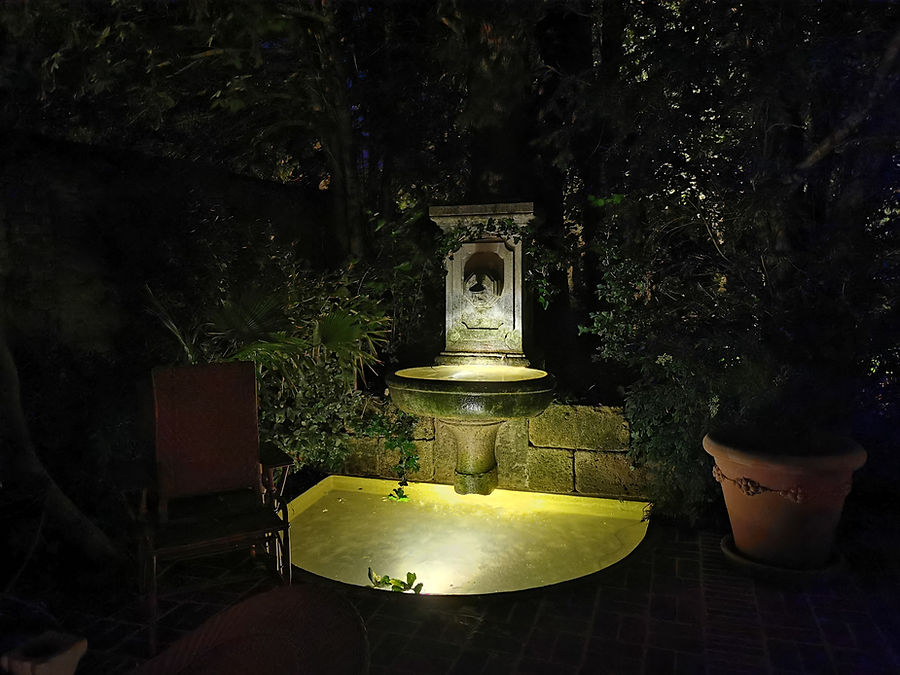 Beleuchteter Steinbrunnen mit Wasserbecken in einem Innenhof bei Nacht