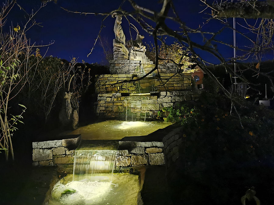 Beleuchtete Natursteinkaskade mit Skulptur und Wasserfall bei Nacht