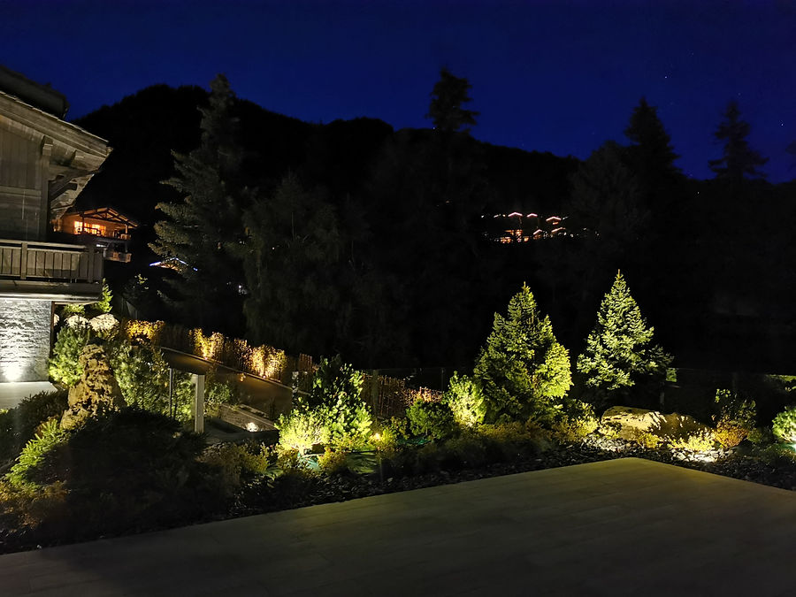 Chalet-Garten in den Bergen mit angestrahlten Nadelbäumen und Felsen bei Nacht