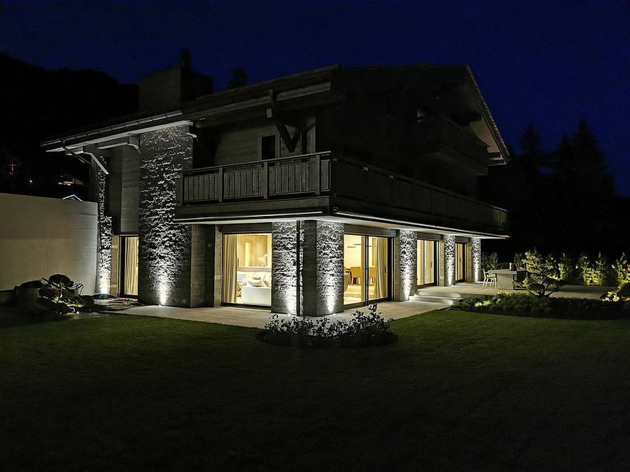 Chalet mit im Streiflicht beleuchteten Natursteinpfeilern bei Nacht